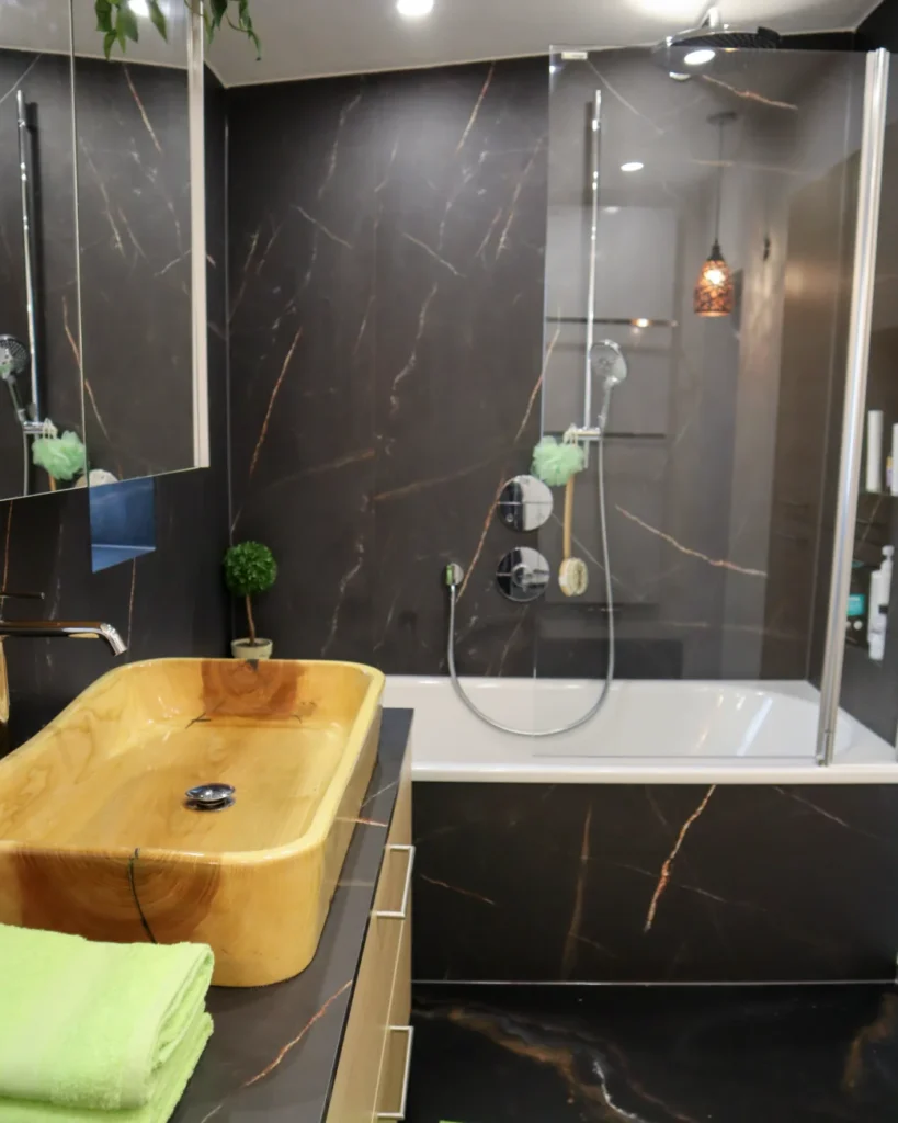 Fugenloses Bad mit dunklen Wandpaneelen, Badewanne und Waschtisch – moderne Badgestaltung im Waldviertel und Weinviertel.