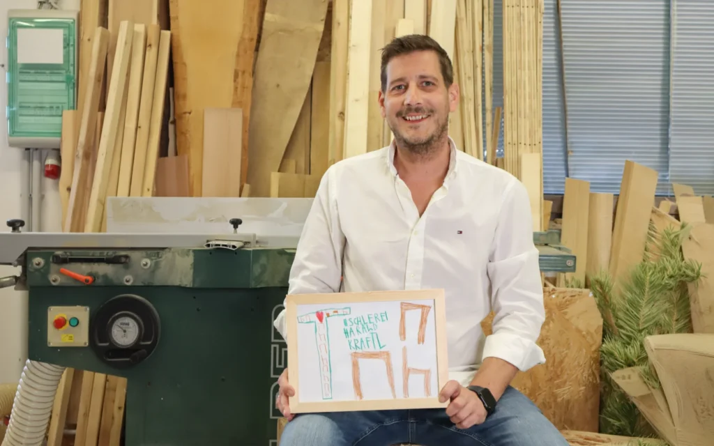 Harald Kraftl mit einem selbst gezeichneten Firmenschild aus seiner Kindheit in der Werkstatt von Einrichtungsprofi Harald Kraftl in Irnfritz.